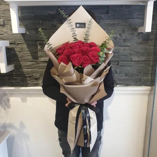 Hand Bouquet With Red Roses And Green Leaves