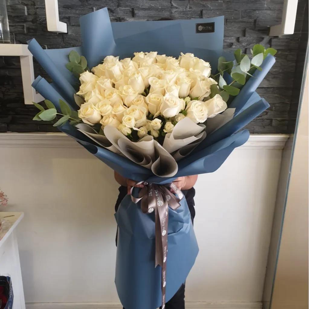 Hand Bouquet With White Roses In Blue Paper Wrapping